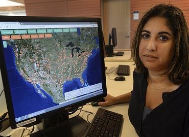 photo of Roopika Risam seated at a computer with screen displaying a large map